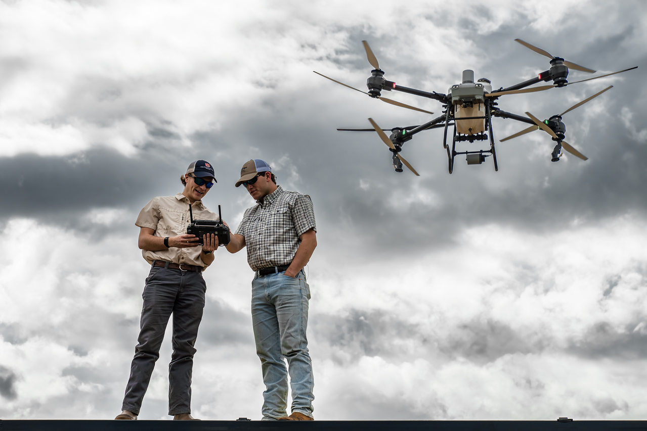 John Hixon and Carter Engle checking the flight controller while their spray drone hovers behind them