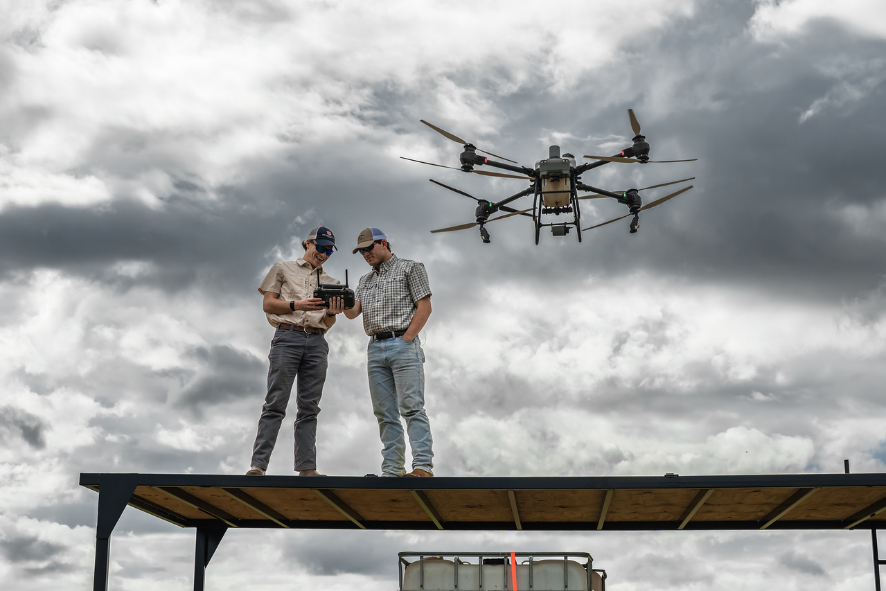 John Hixon and Carter Engle on their launch platform with the spray drone hovering overhead